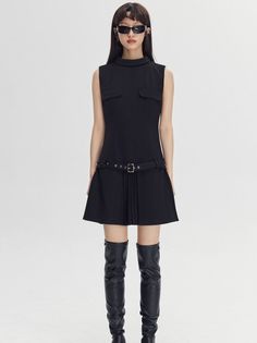 Woman in a black dress, sunglasses, and thigh-high boots in a studio setting