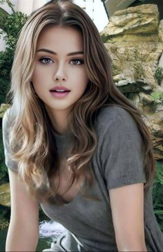 Woman with long brown hair wearing a v-neck shirt outdoors with rocks and greenery