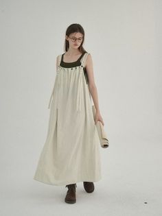 Woman in a long cream dress and glasses holding a rolled-up fabric