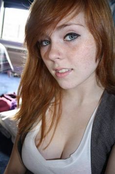 Young woman with red hair and freckles wearing a white top indoors