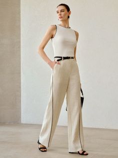 Woman in a white sleeveless top and wide leg pants with a black belt
