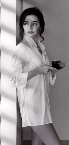 Woman in a white shirt holding a cup, with soft lighting and exposed skin