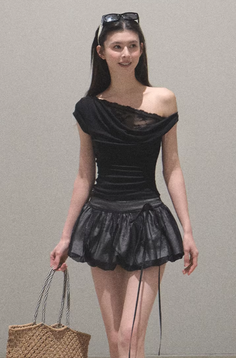 Woman in a black off-shoulder top and mini skirt holding a wicker bag