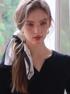 Woman with long hair and a black top, wearing a hair scarf and gold earrings