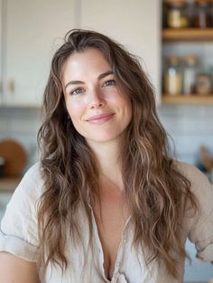 Woman with long wavy hair and green eyes in a light shirt in a kitchen