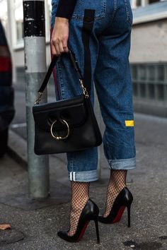 Person in blue jeans, fishnet stockings, and high heels holding a black handbag