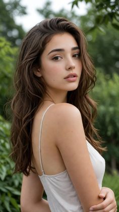 Woman with long wavy hair in a white camisole looking over her shoulder