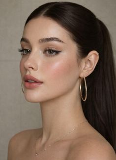 Woman with dark hair in a ponytail wearing hoop earrings and a necklace