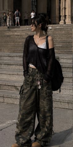 Woman in camouflage pants and a black mesh top standing outdoors