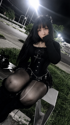 Woman in gothic attire with a corset and thigh-high stockings sitting outdoors at night