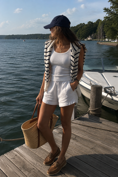 Woman in a baseball cap and white shorts standing on a dock by a lake