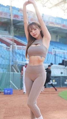 Woman in a sports bra and leggings stretching on a baseball field