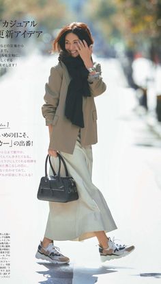Woman in a blazer, scarf, and long skirt walking outdoors and smiling