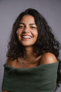 Woman with long dark hair wearing an off-shoulder green top, smiling at the camera
