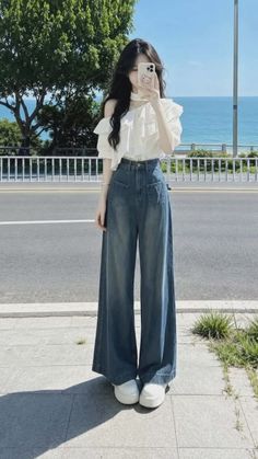 Woman in an off-shoulder top and wide-leg jeans taking a selfie by the ocean