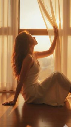 Woman in a white dress sitting on the floor by a window at golden hour