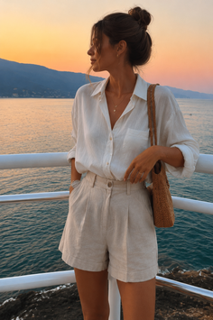 Woman in a white linen shirt and shorts by the sea at golden hour