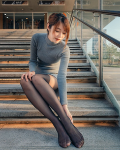 Woman in a gray dress and black pantyhose sitting on outdoor stairs