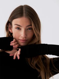 Woman with long brown hair and blue eyes wearing a black top and gold hoop earrings