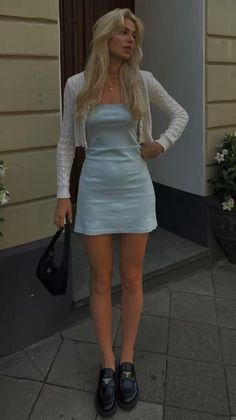 Woman with blonde hair in a light blue mini dress and white cardigan outdoors