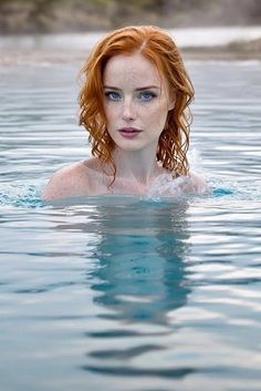 Woman with red hair and freckles in water, looking directly at the viewer
