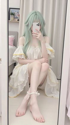 Person with mint green hair in a white dress taking a mirror selfie indoors