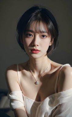 Woman with short black hair wearing a white top and necklace