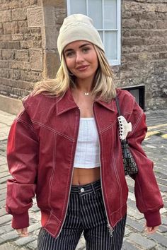 Woman in a red jacket, white crop top, and striped pants on a street