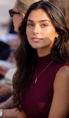 Woman with long dark hair wearing a burgundy top and cross necklace