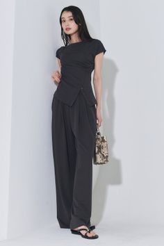 Woman with long black hair wearing an asymmetrical top and wide-leg pants