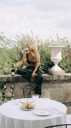 Woman in a green bralette and pants drinking wine on a stone wall