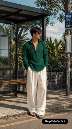 Man in a green shirt and white pants standing at a bus stop