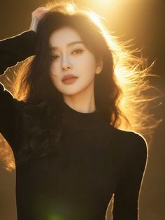 Woman with long black hair in a black top, backlit by golden hour light