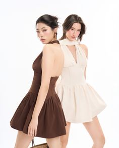 Two women in mini dresses with halter necks posing in a studio