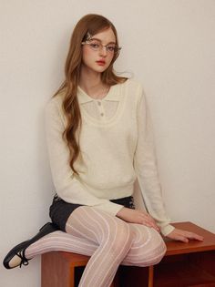 Woman with long hair and glasses wearing a white sweater and patterned tights