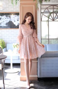 Woman in a pink lace dress with ruffle sleeves standing indoors