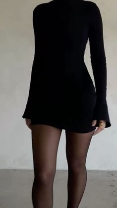 Woman in a black long-sleeved dress and tights indoors