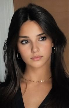 Young woman with long dark hair wearing hoop earrings and a gold necklace
