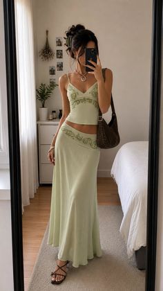 Woman in a light green two-piece outfit taking a mirror selfie indoors