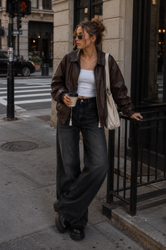 Woman in a brown leather jacket and wide leg jeans on a city street