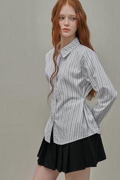 Woman with long red hair and freckles wearing a striped shirt and black skirt