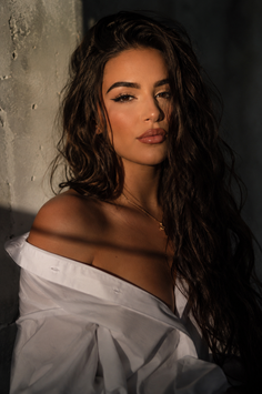 Woman with long dark hair wearing an unbuttoned white shirt in dramatic lighting