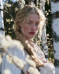 Woman with blonde braided hair and freckles among birch trees with white blossoms