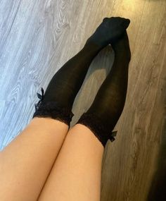 Legs wearing black thigh-high socks with lace trim and bows on a wooden floor