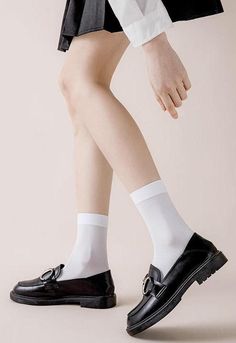 Person wearing white socks and black loafers with a short skirt and white shirt