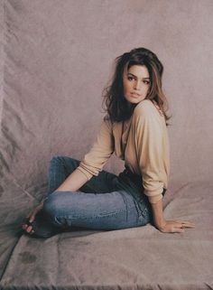 Woman with long hair wearing jeans and a cardigan, sitting on a draped fabric background