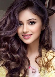 Woman with long wavy brown hair and pink lipstick wearing a gold top