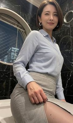 Woman in a light blue shirt and grey skirt with a cityscape at night in the background