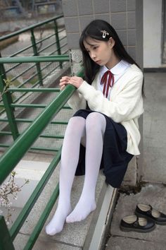 Young woman in a school uniform and white tights sitting outdoors