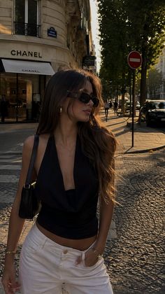 Woman in a black top and white pants on a sunlit street at golden hour